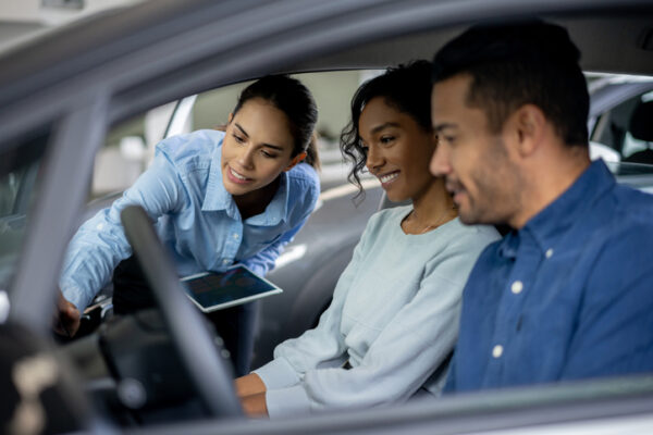 Saleswoman working at a dealership showing a car to a happy couple and trying to make a sale - business concepts